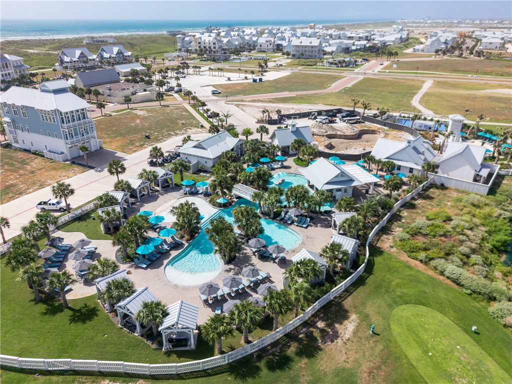 Aerial view of a resort-style pool complex with cabanas, homes, and ocean beyond.