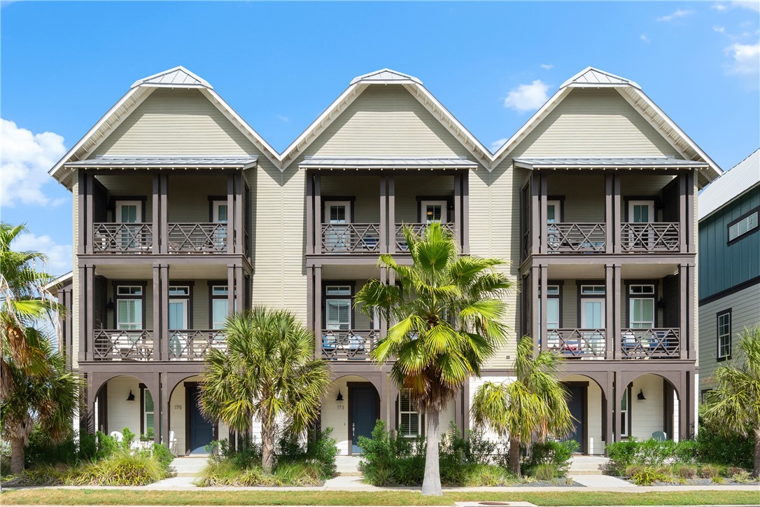 Three-story townhome exterior with stacked balconies, peaked roof sections, and tropical landscaping.