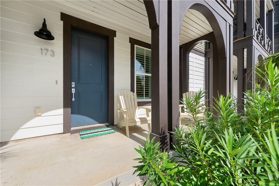 Home entrance with a blue door marked 173, a covered arched porch, chairs, and leafy landscaping.