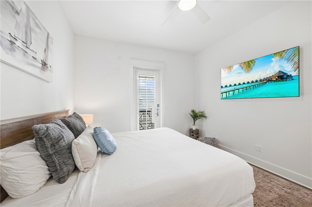 Bright bedroom with a large white bed, layered pillows, and a shuttered glass door.