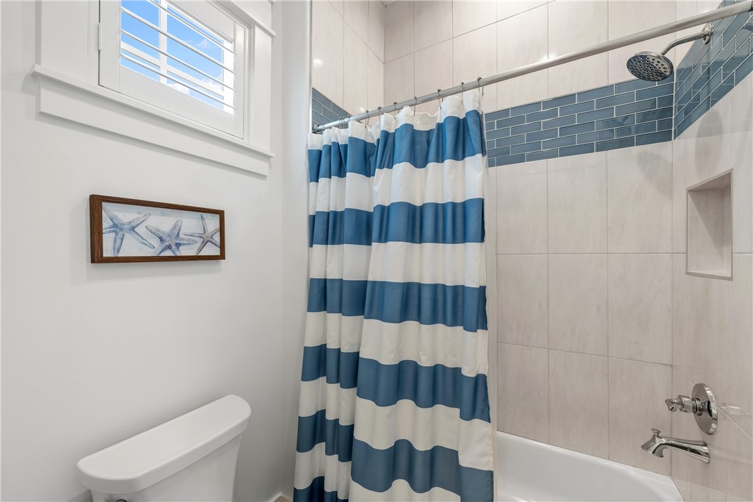 Bathroom with a blue-and-white striped shower curtain, tiled tub surround, and high shuttered window.