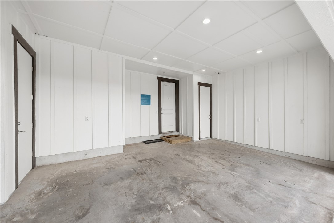 Empty garage with a bare concrete floor, white paneled walls, and several doors.