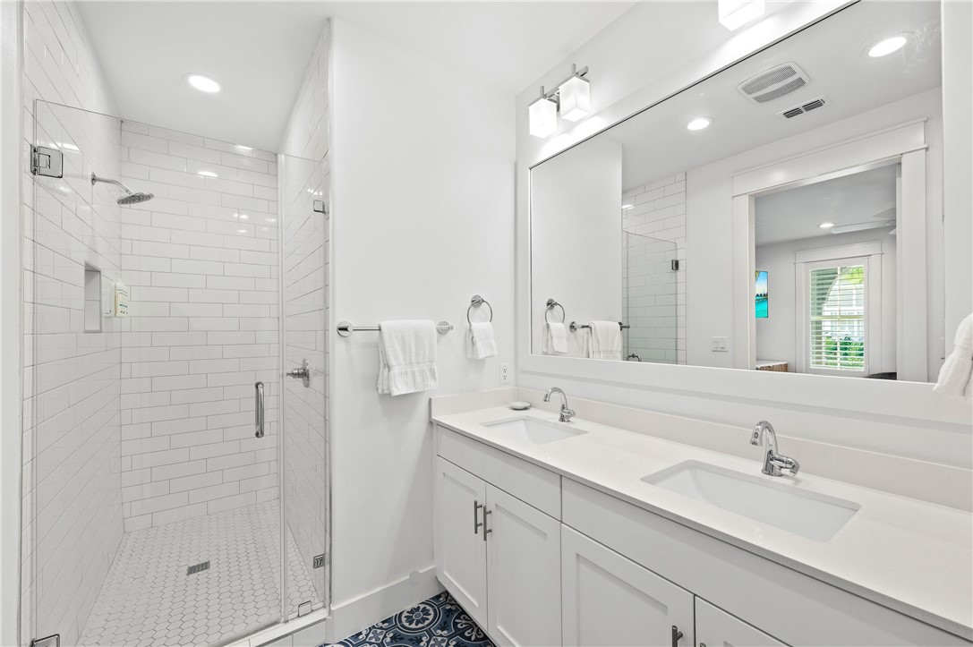 Bathroom with a glass-enclosed subway-tile shower and double-sink vanity above patterned blue floor tile.