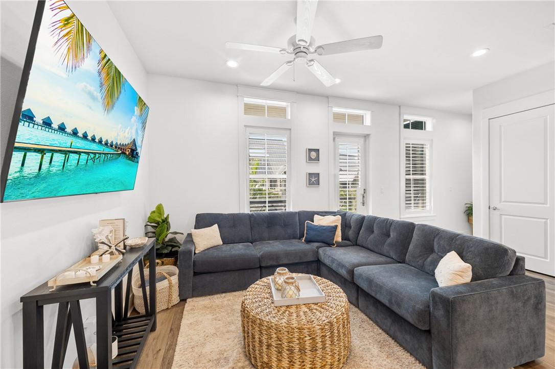 Furnished living room with a gray sectional sofa, woven coffee table, and beach scene on the wall-mounted screen.