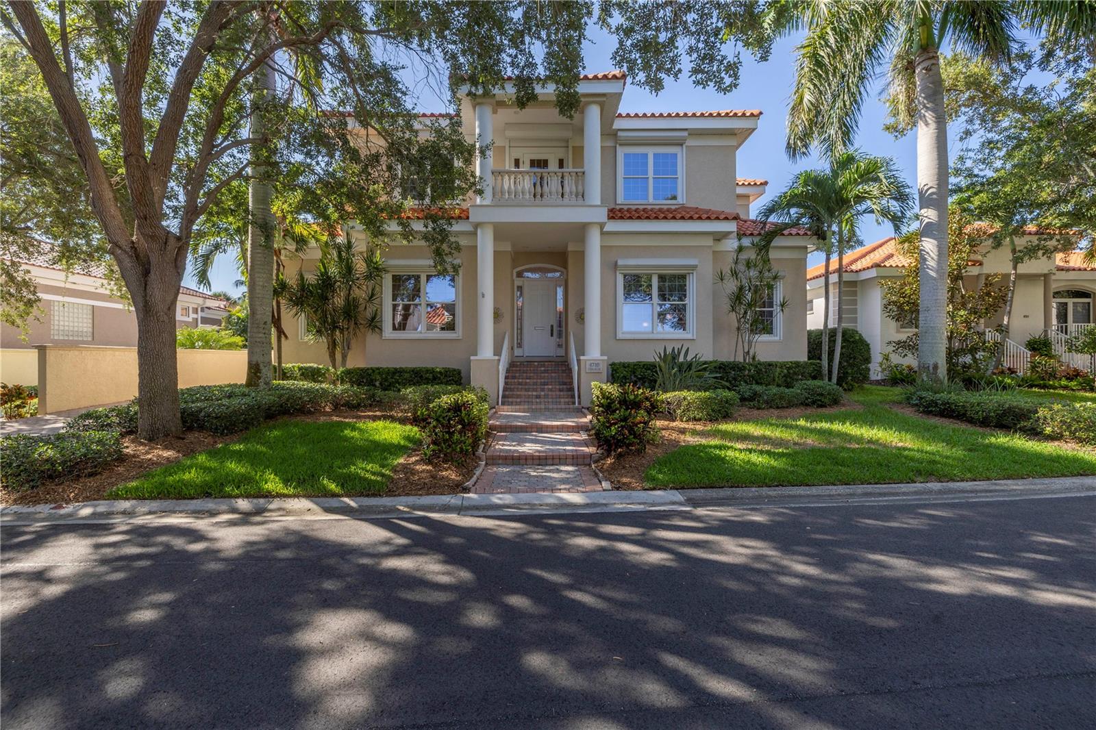 Two-story stucco home with a columned entry, red tile roof, and palm-lined lawn.