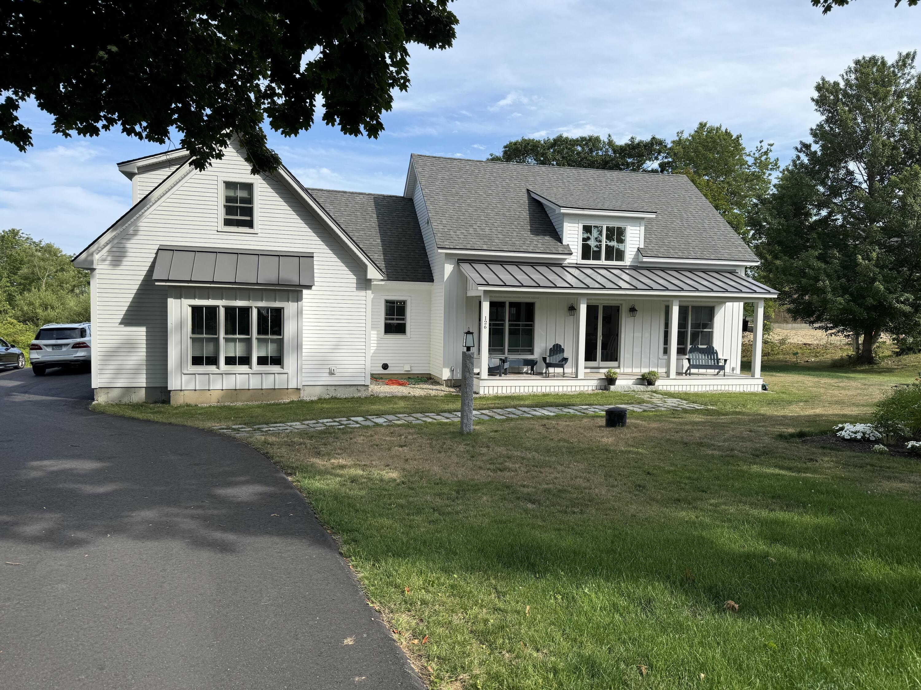 White two-story house with a covered porch, gray roof, and broad front lawn.