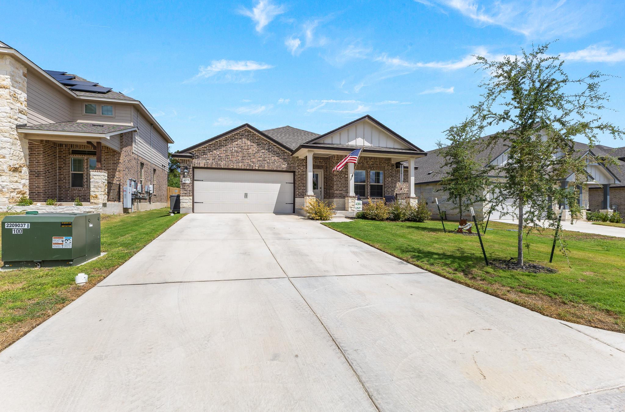 Brick home with a two-car garage, covered porch, American flag, and broad concrete driveway.
