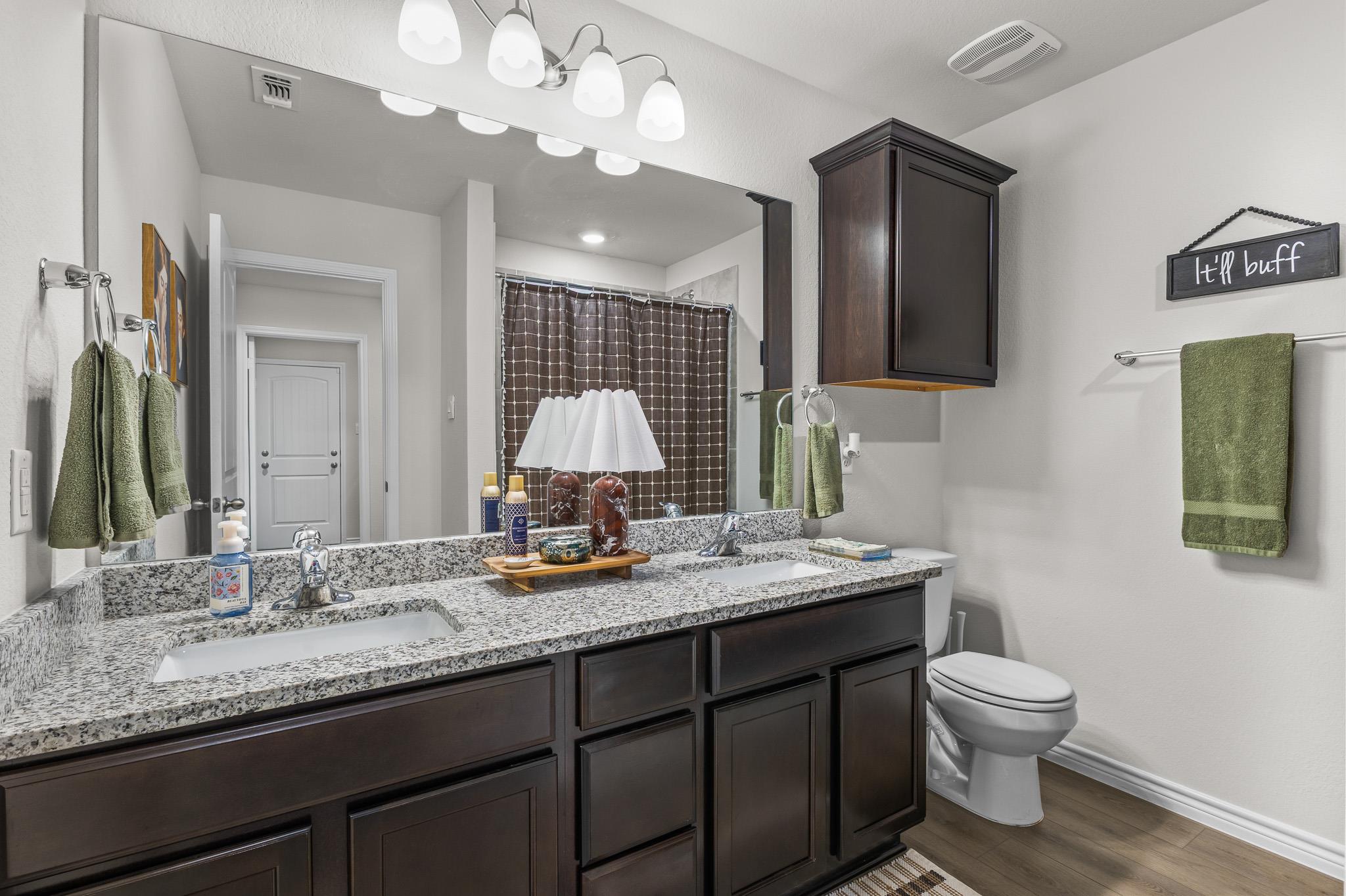Bathroom with a dark double vanity, speckled granite countertop, and brown checked shower curtain.