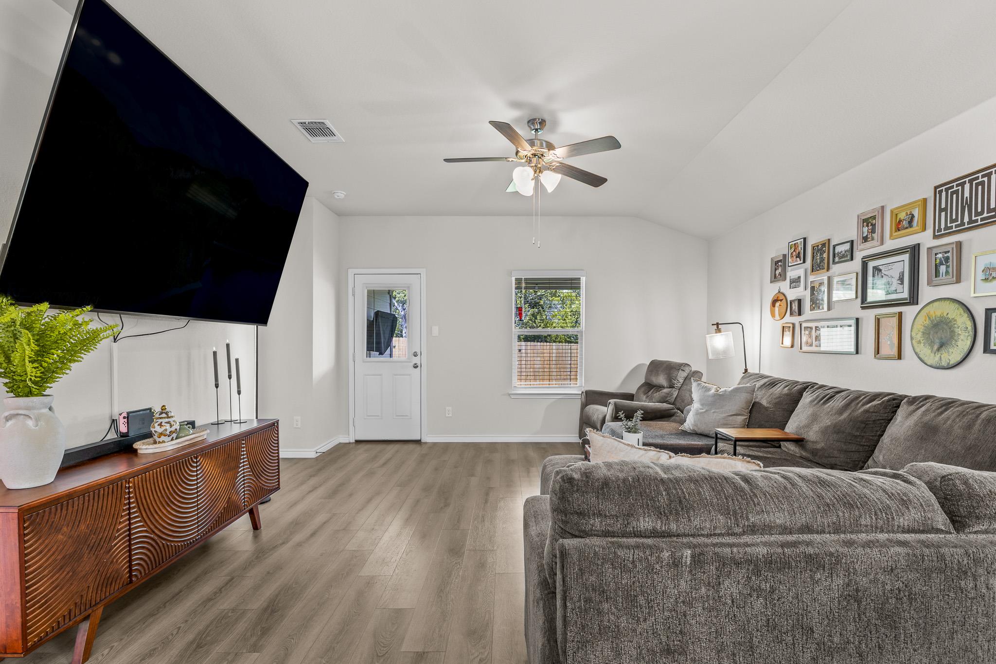 Living room with gray sectional sofas, a large television, wood-look floors, and a gallery wall.