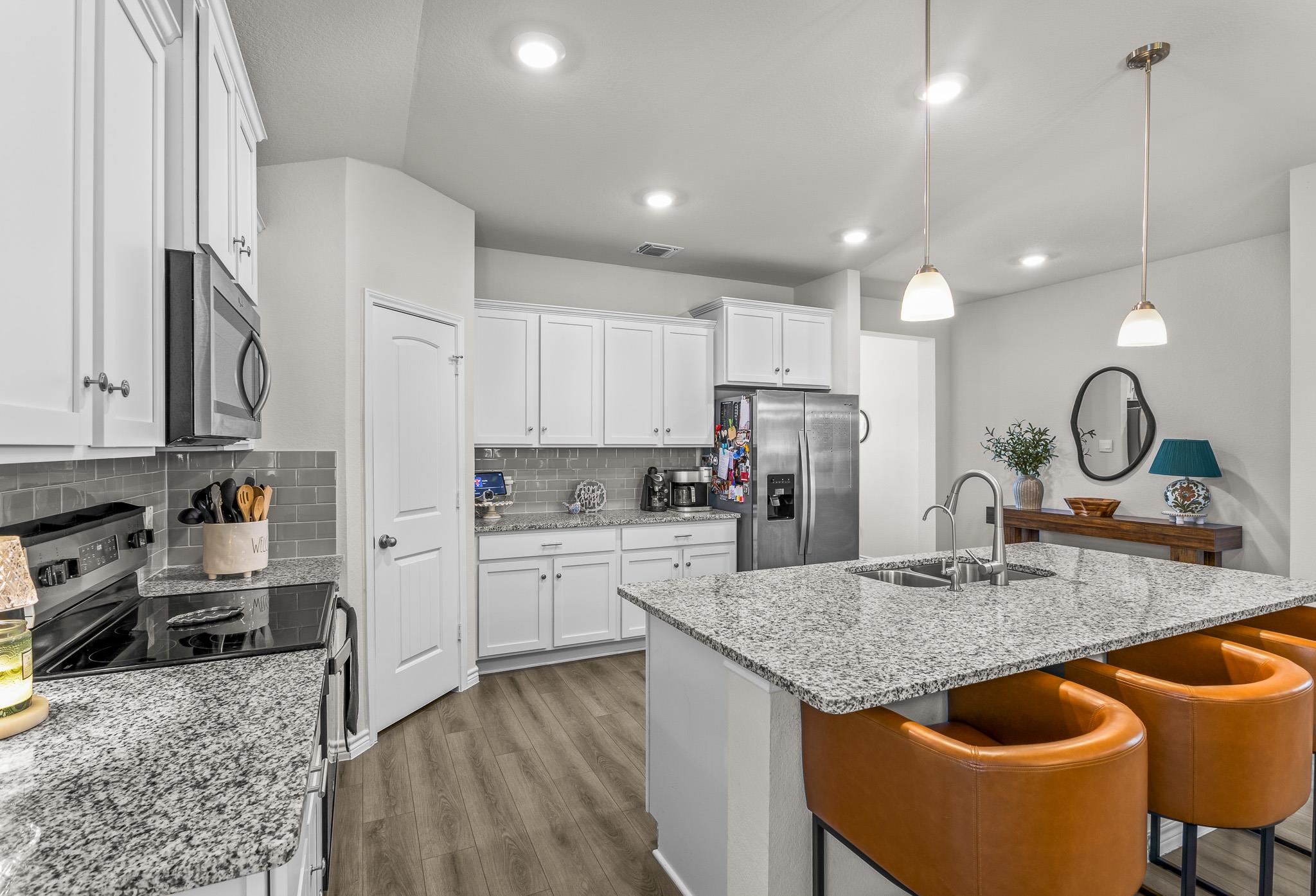 Kitchen with white cabinets, granite island, stainless steel appliances, and brown leather bar stools.
