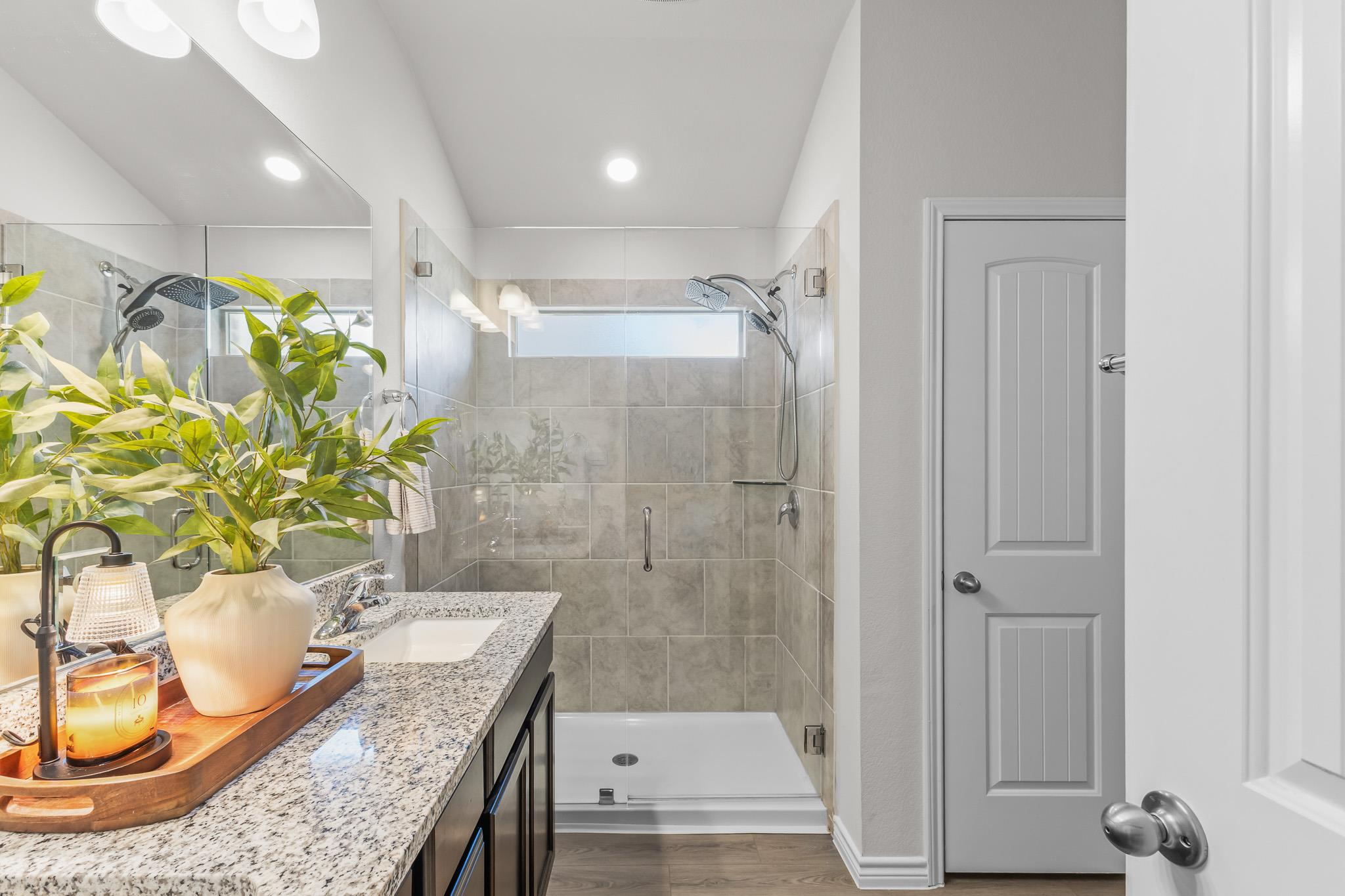 Bathroom with a glass-enclosed tiled shower and granite vanity decorated with plants and a candle.