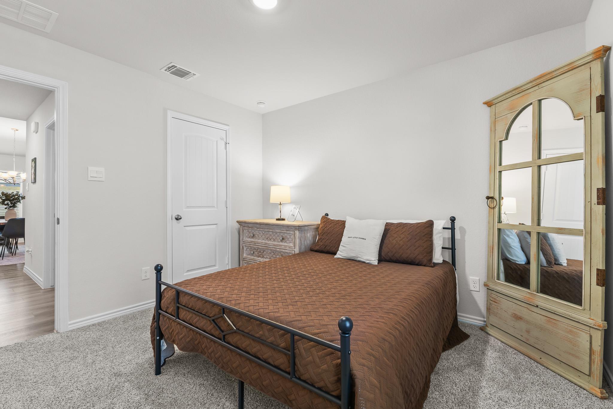 Staged bedroom with a brown-quilted bed, distressed wood dresser, and tall mirrored wardrobe.