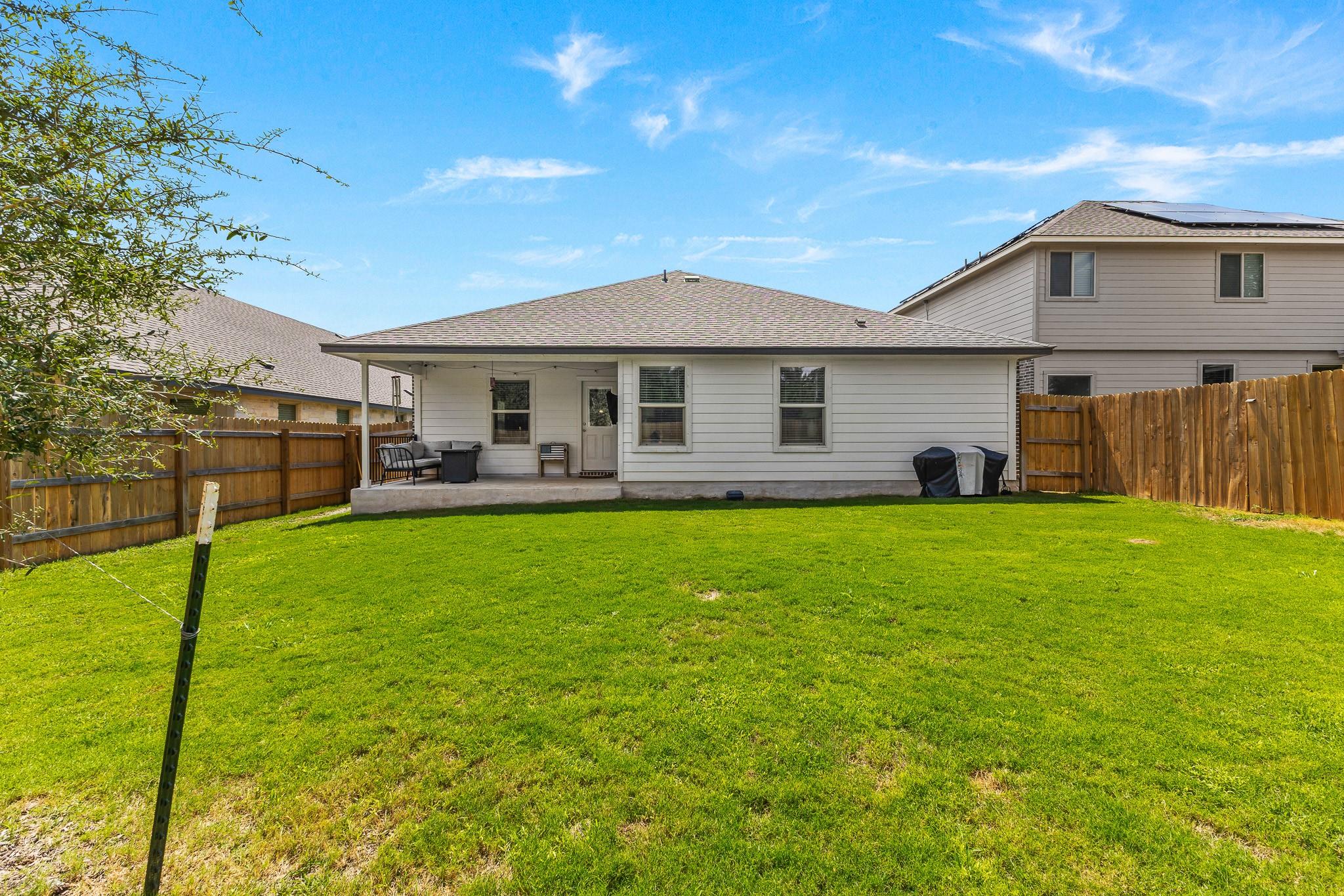 Backyard lawn and fenced rear of a single-story home with a covered patio.