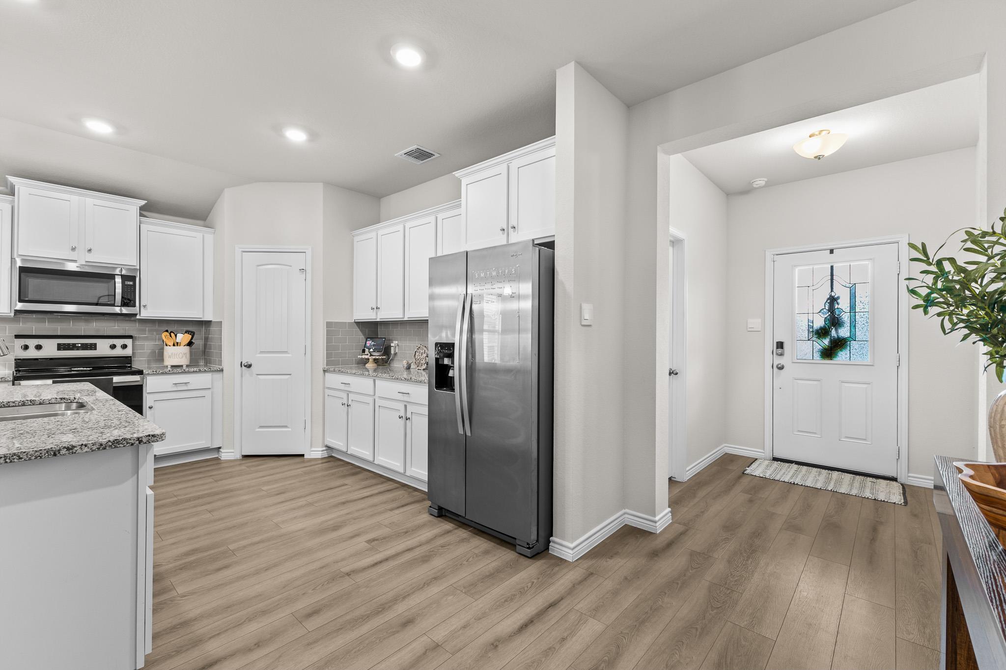 Kitchen with white cabinets, granite counters, stainless steel appliances, and an adjoining entry with a decorative glass door.