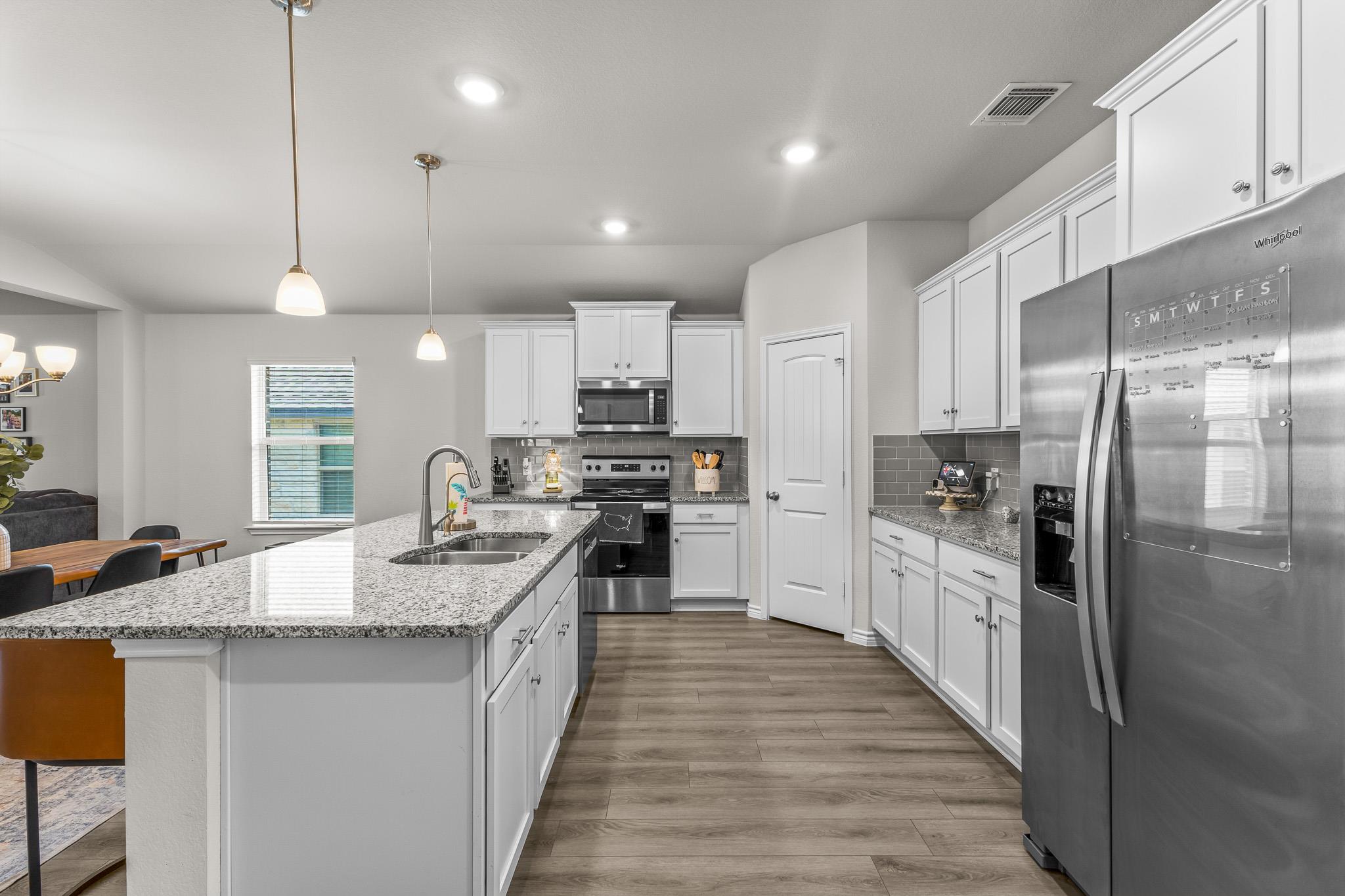 Kitchen with white cabinets, granite island, gray tile backsplash, and stainless steel appliances.