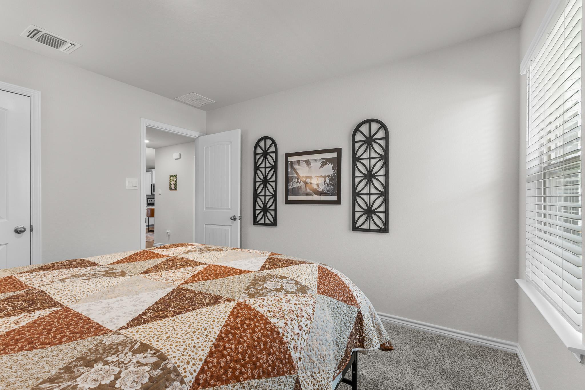 Bedroom with a patchwork quilt on the bed and white blinds over a large window.