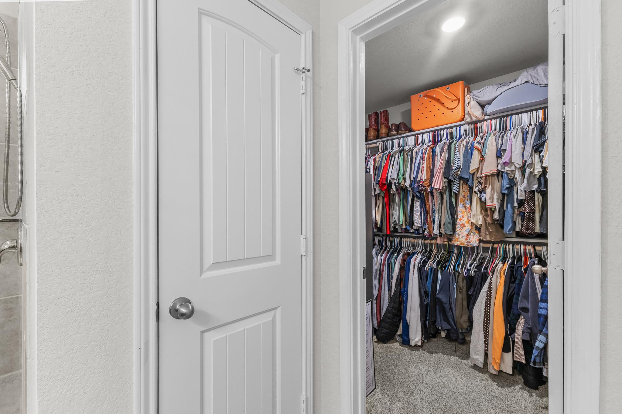 Walk-in closet with two rows of hanging clothes and storage on the upper shelf.