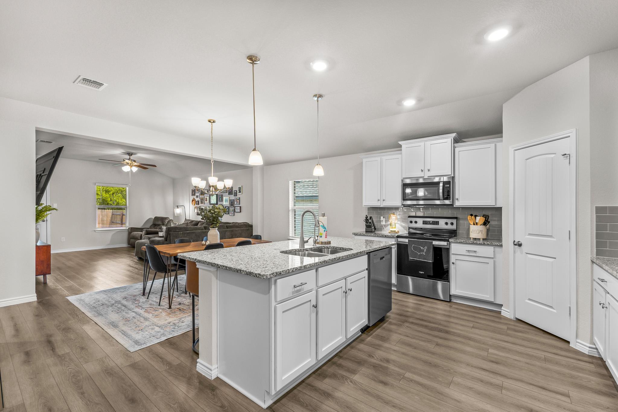 Open-plan kitchen with a large granite island, white cabinets, and a living area beyond.