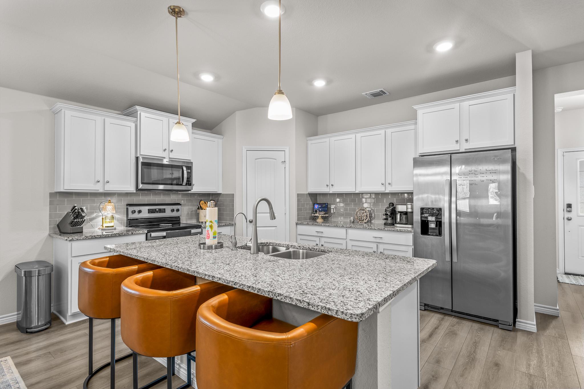 Kitchen with a granite island, three orange-brown bar stools, white cabinets, and stainless steel appliances.