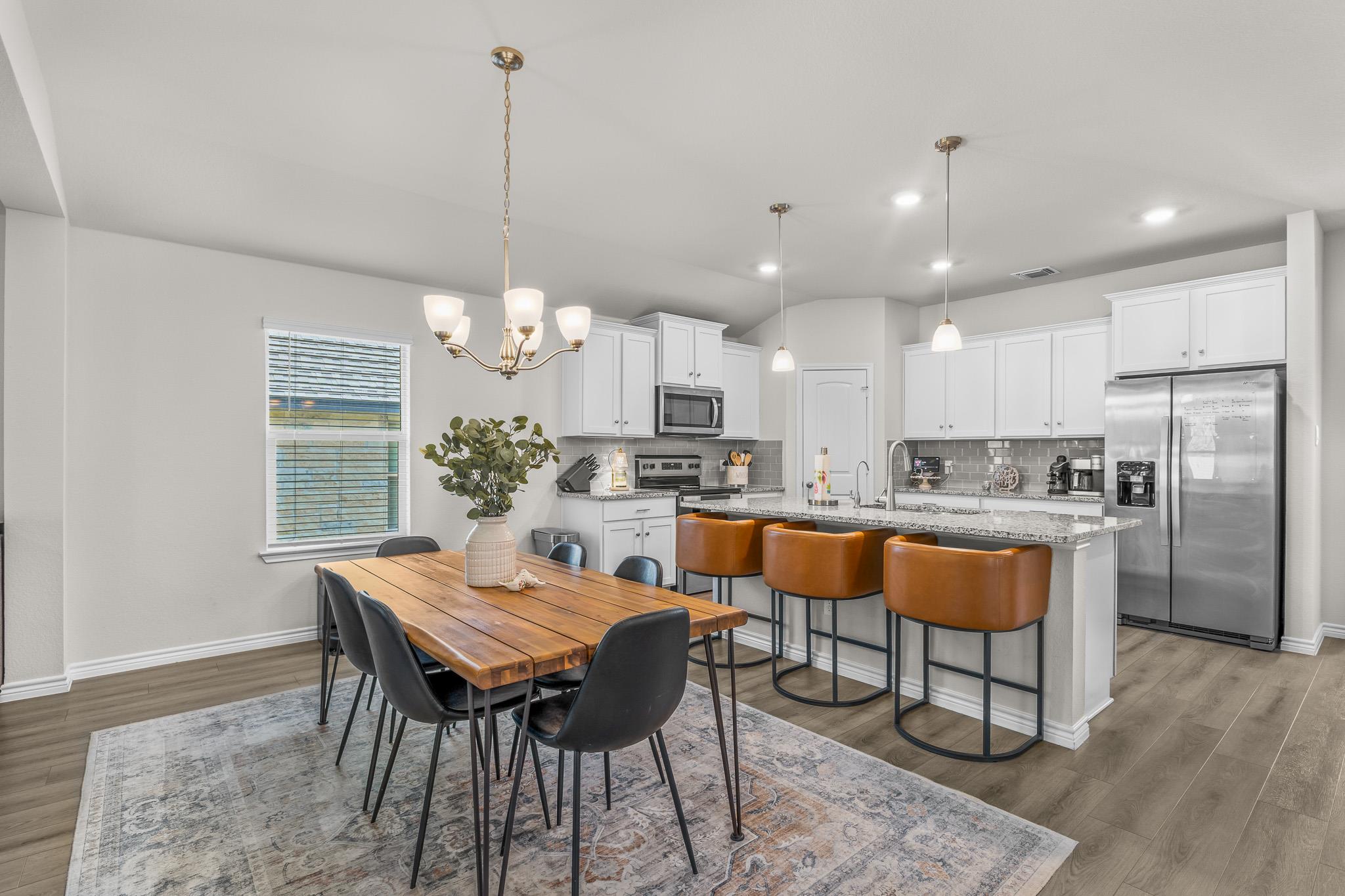 Bright open kitchen and dining area with white cabinets, island seating, and wood dining table.
