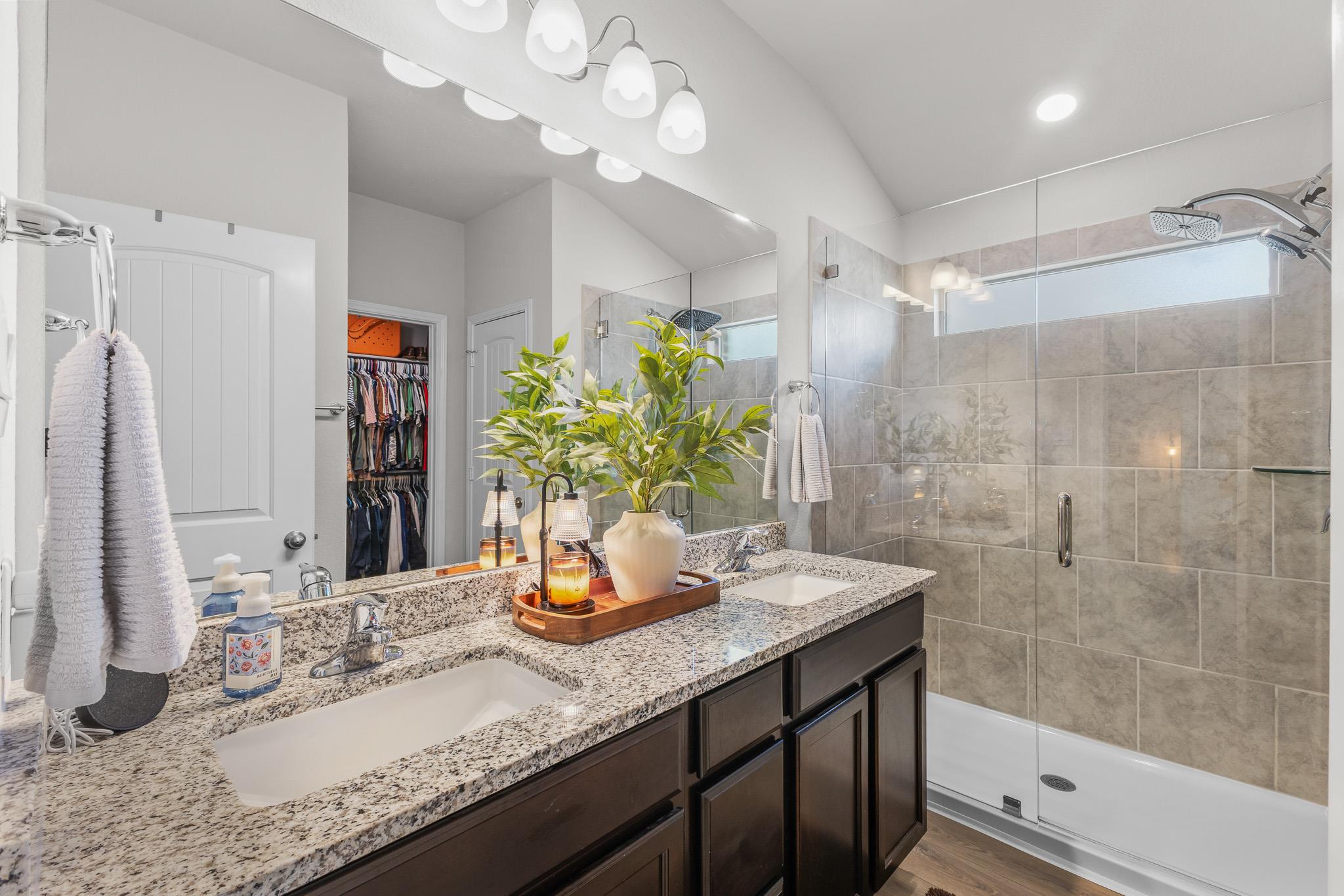 Bathroom with a granite double vanity and a glass-enclosed tiled shower.