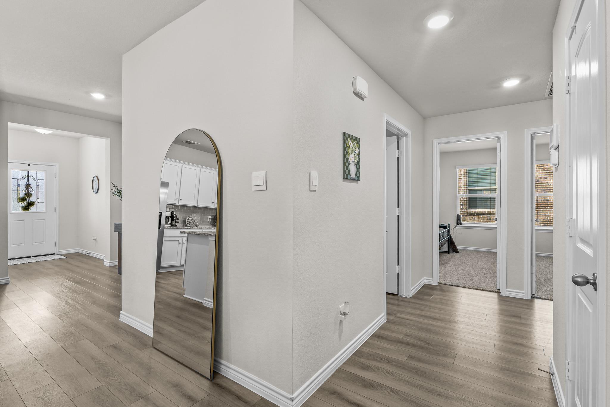 Entry hallway with gray wood-look floors, an arched mirror, and doorways to carpeted rooms.