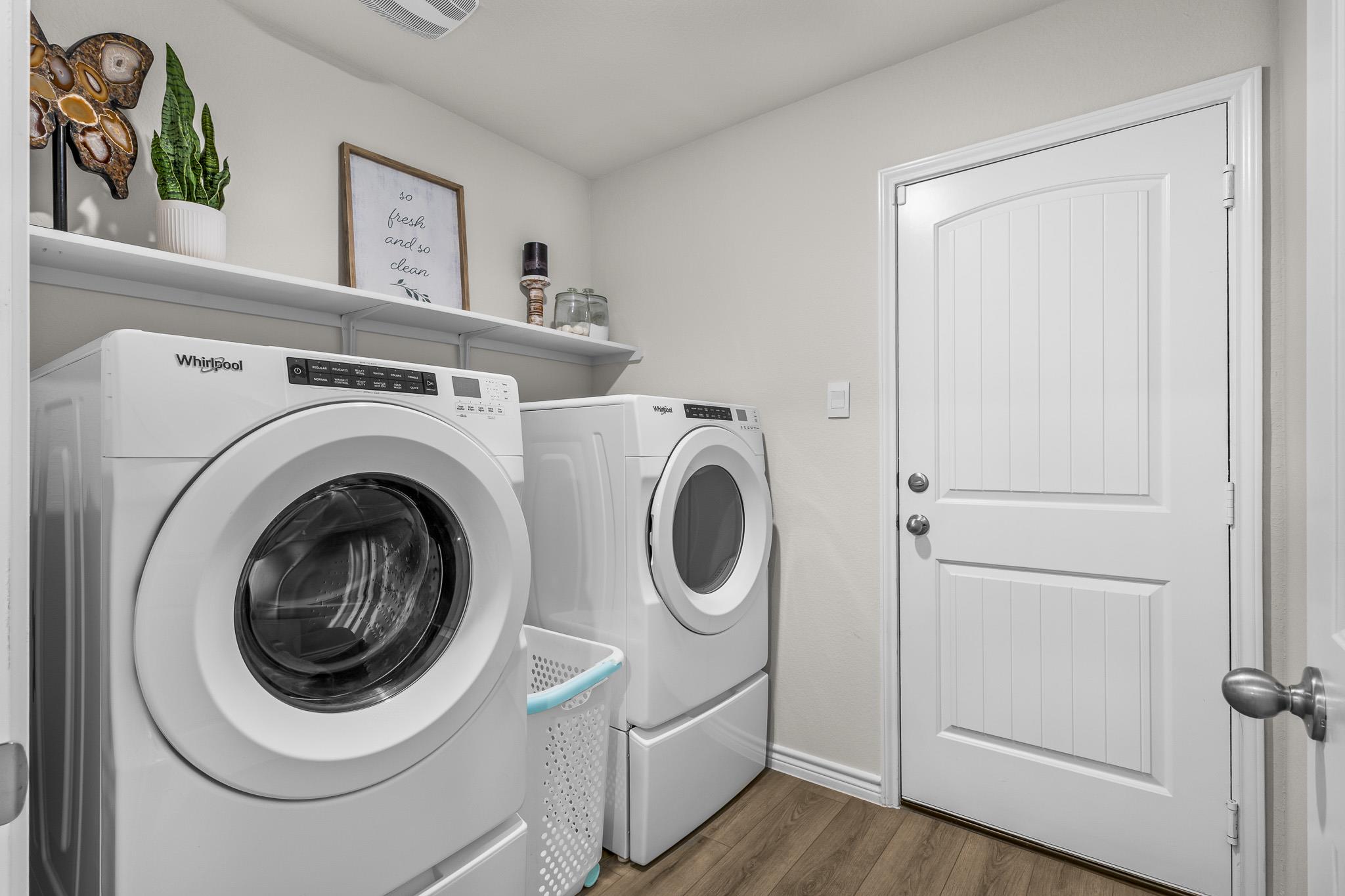 Laundry room with a front-loading washer and dryer, wall shelves, and a white paneled door.