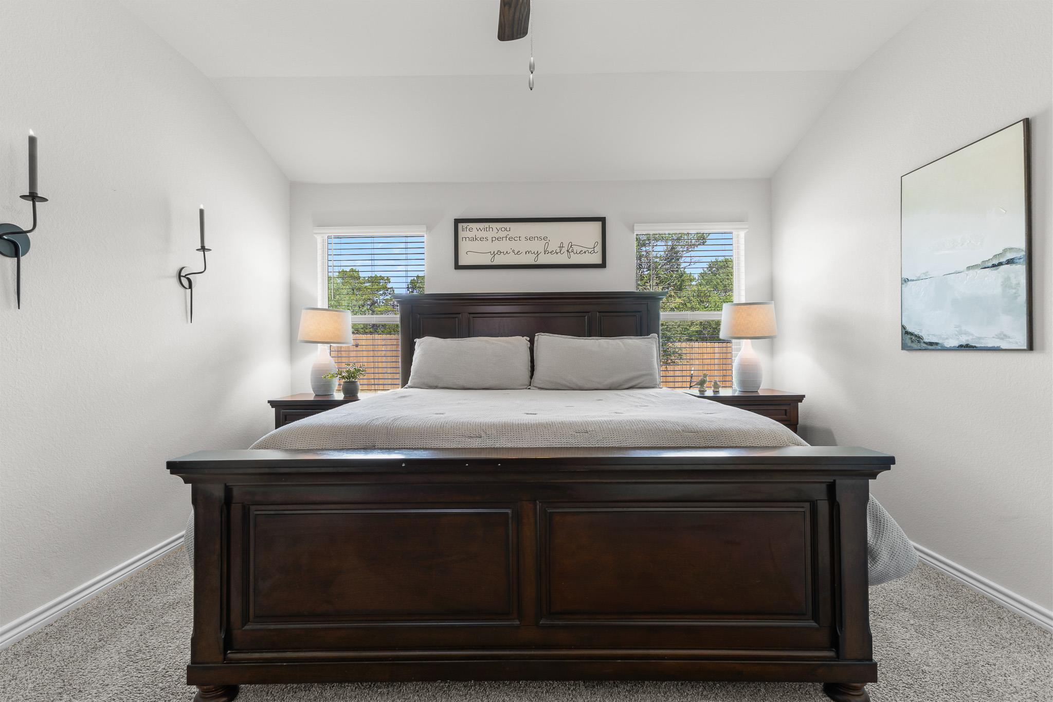 Bedroom with a large dark wood bed centered between two windows and matching bedside lamps.