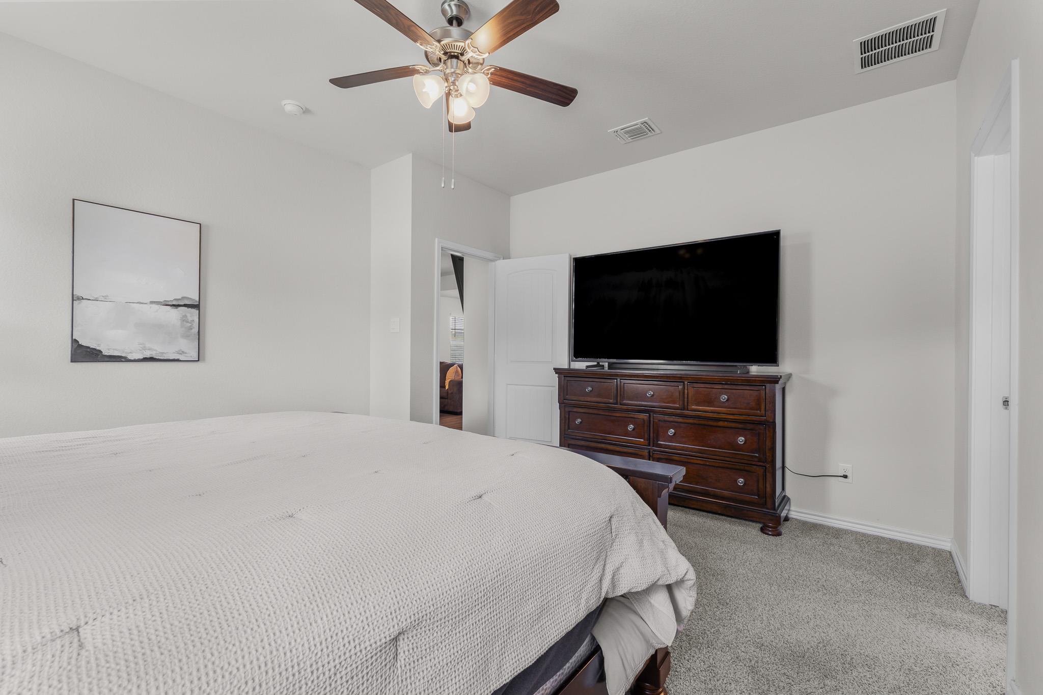 Bedroom with a large bed, dark wood dresser and television, and ceiling fan.