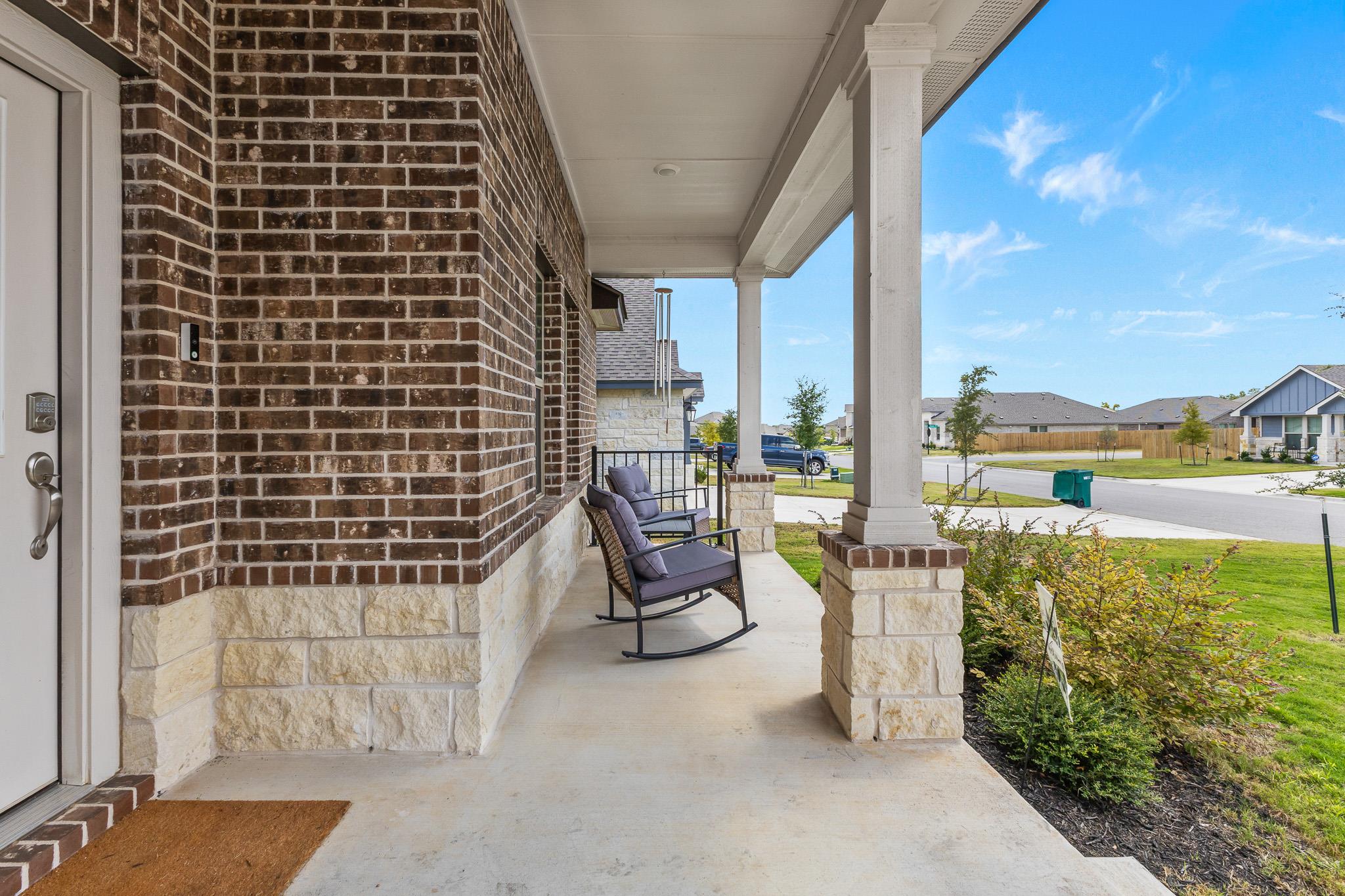 Covered front porch with cushioned rocking chairs, brick and stone walls, and white columns.