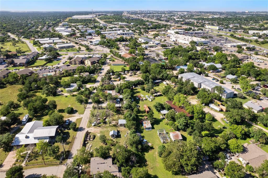 Aerial view of open land among homes and commercial buildings in a tree-lined area.