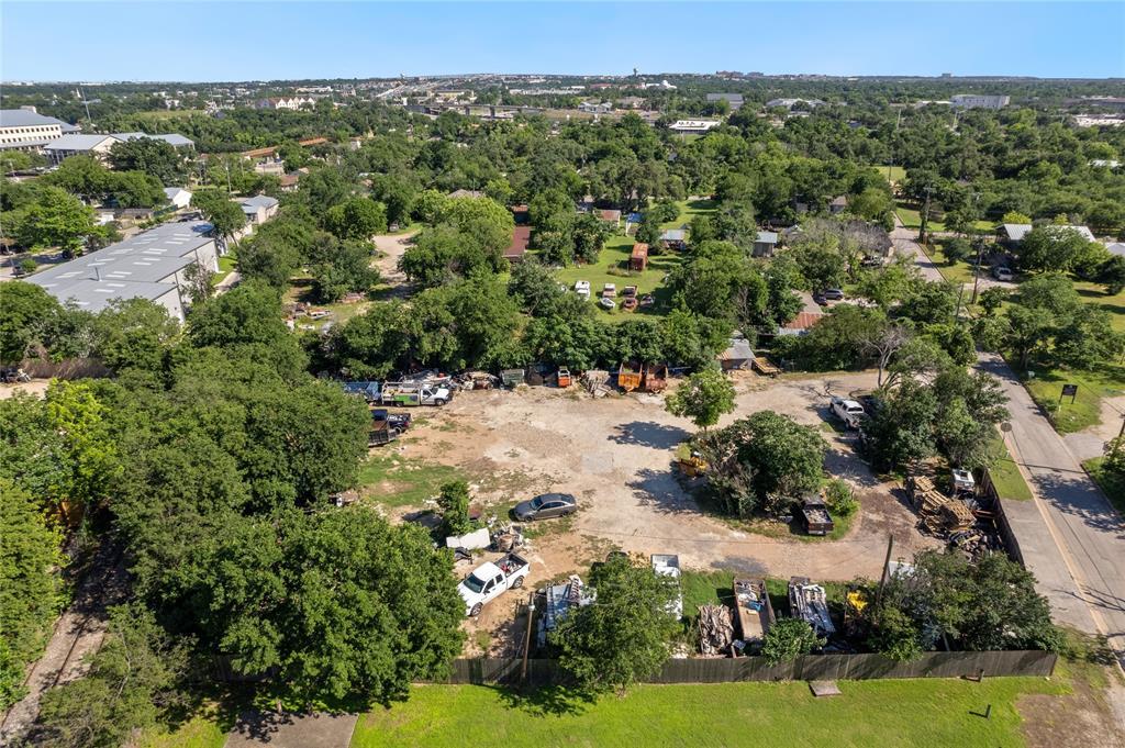 Aerial view of a cleared lot with mature trees, vehicles, and construction materials.