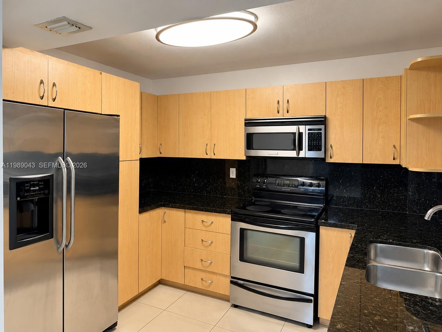 Kitchen with light wood cabinets, black countertops, stainless steel appliances, and a double-basin sink.