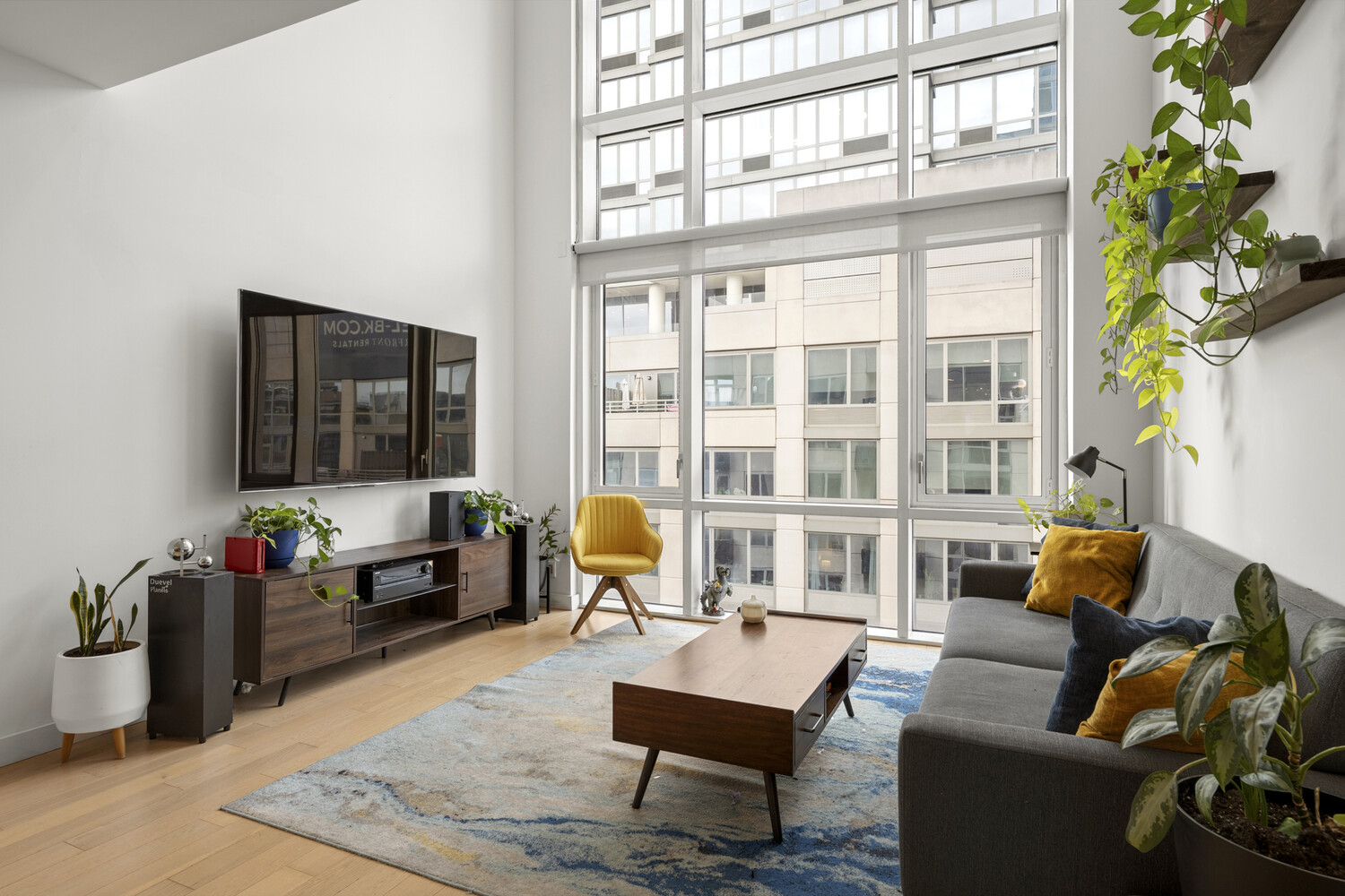 Living room with floor-to-ceiling windows, a gray sofa, and a mustard-yellow accent chair.