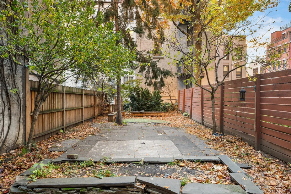 Paved backyard courtyard with wooden fences, trees, and fallen autumn leaves.
