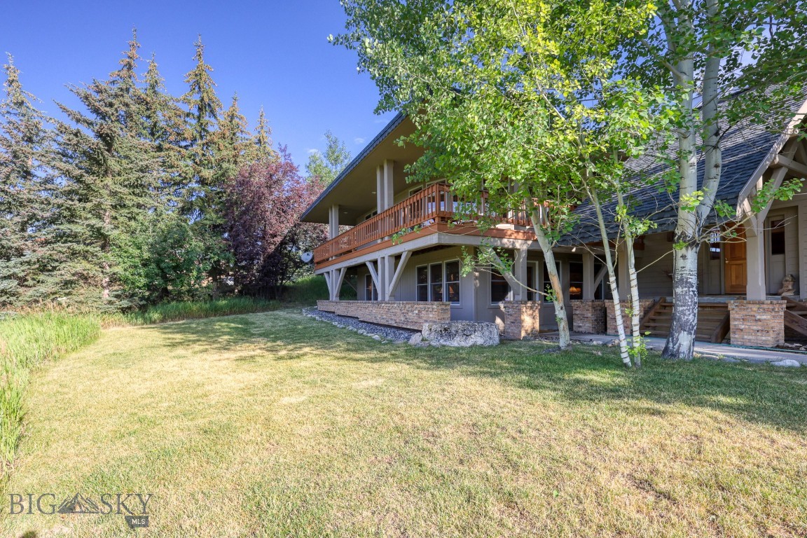 Montana home with a raised wooden balcony, brick foundation, and tree-lined lawn.