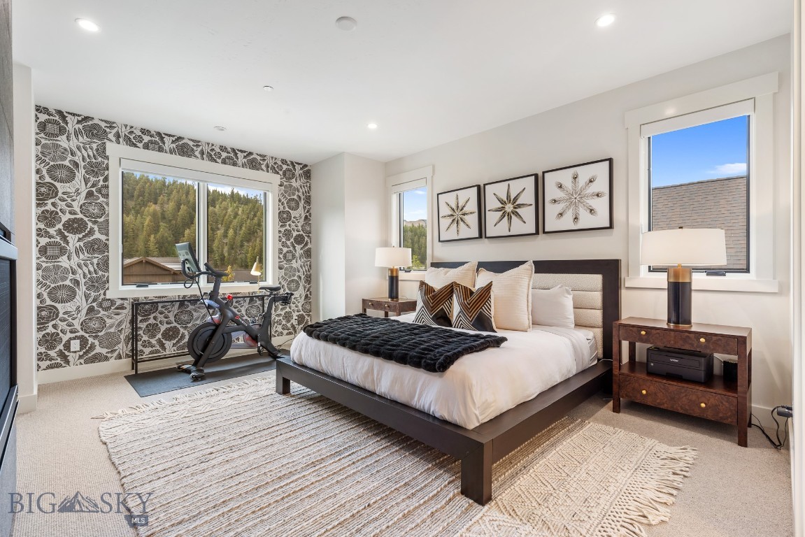Staged bedroom with a patterned accent wall, exercise bike, and wooded hillside visible through the window.