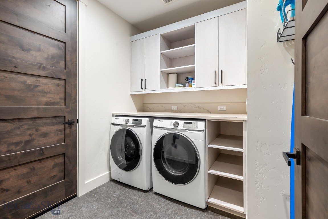 Laundry room with front-loading washer and dryer, white cabinets, and open storage shelves.
