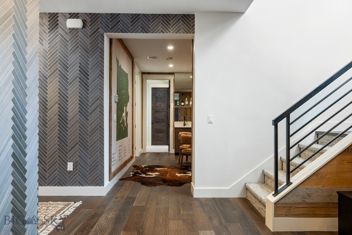 Entryway with a patterned accent wall, wood floors, and a staircase with black metal railing.