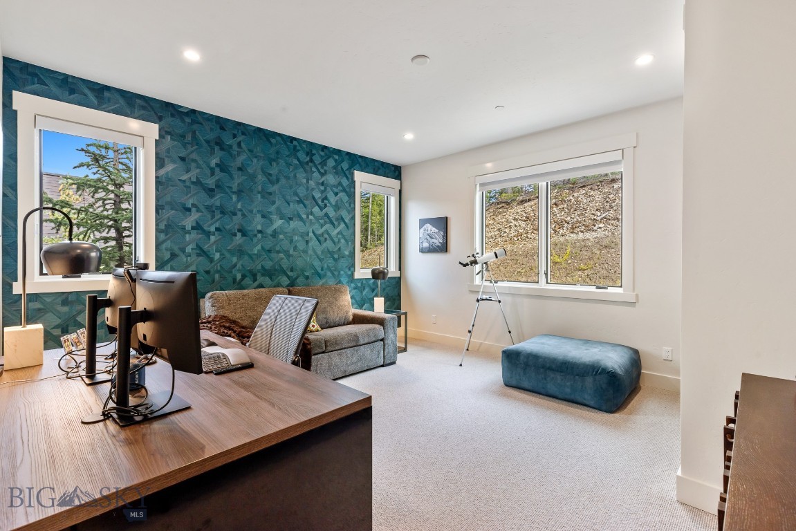 Home office with a wood desk, gray sofa, teal patterned wall, and telescope by the windows.