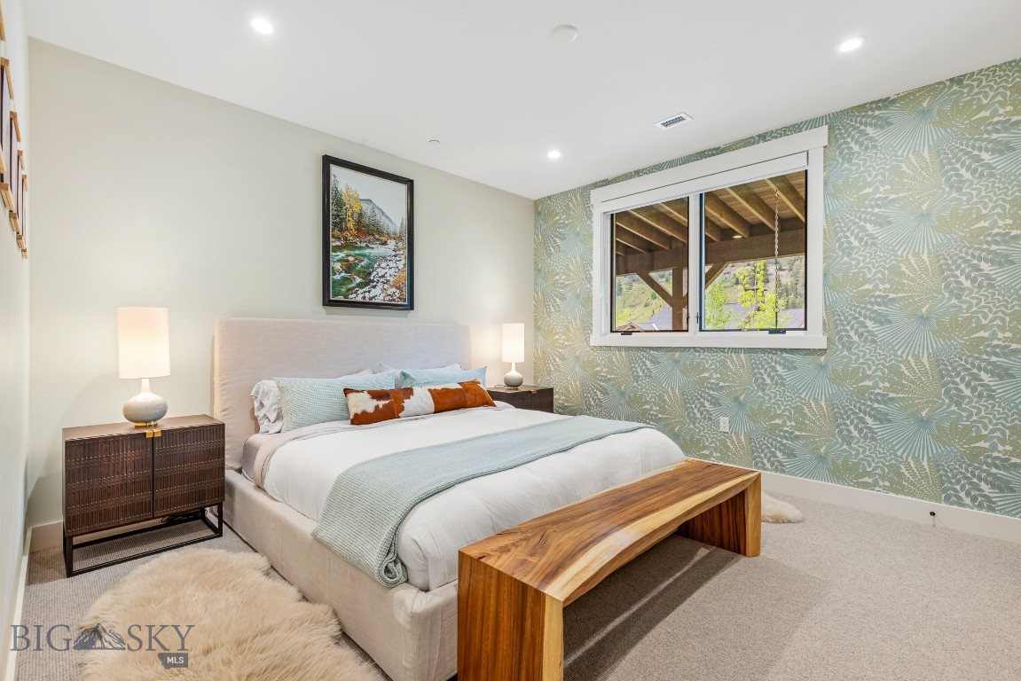 Staged bedroom with pale blue bedding, a wooden bench, and a botanical accent wall beside a window.