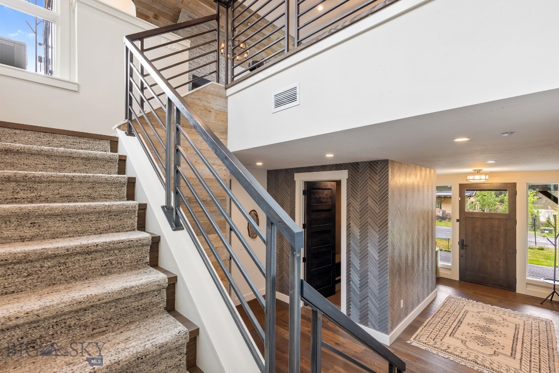 Entryway with carpeted stairs, metal railings, and a wood front door with windows.
