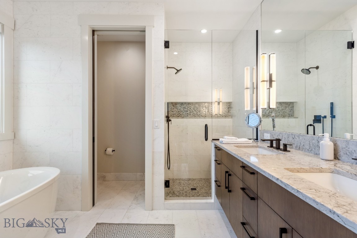Marble bathroom with glass shower, long double vanity, and freestanding tub.