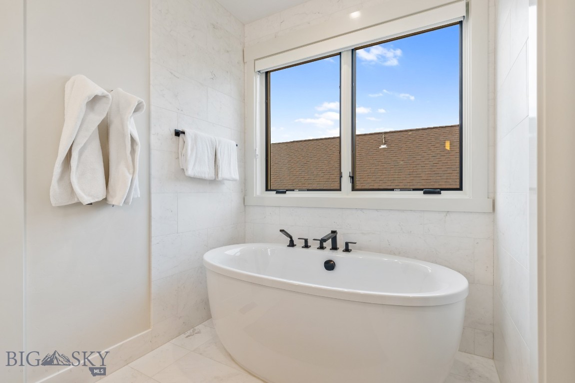 Bathroom with a freestanding white tub, black fixtures, marble-look tile, and a large window.