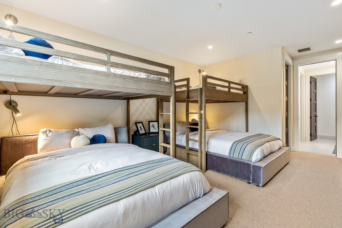 Bedroom with two large beds beneath wooden loft bunks and striped bedding.