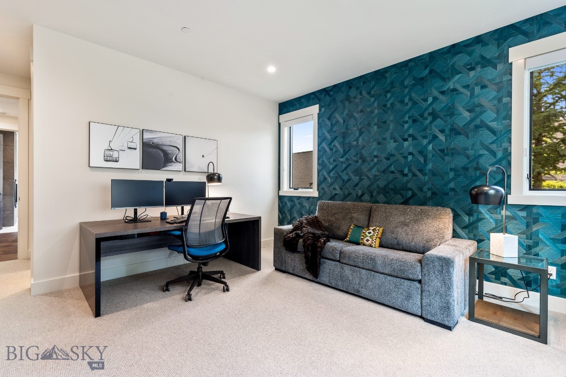 Home office with dual monitors and a gray sofa against teal geometric wallpaper.