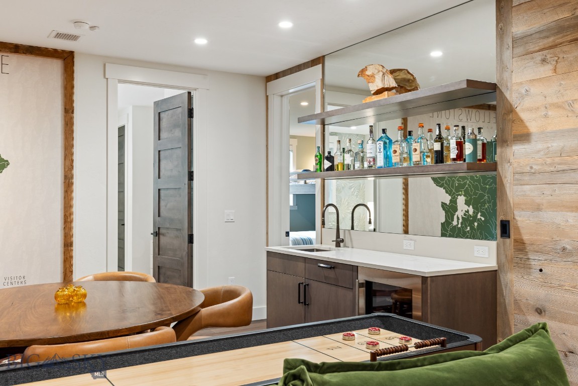 Furnished bar and game area with open liquor shelves, a round dining table, and a shuffleboard table.