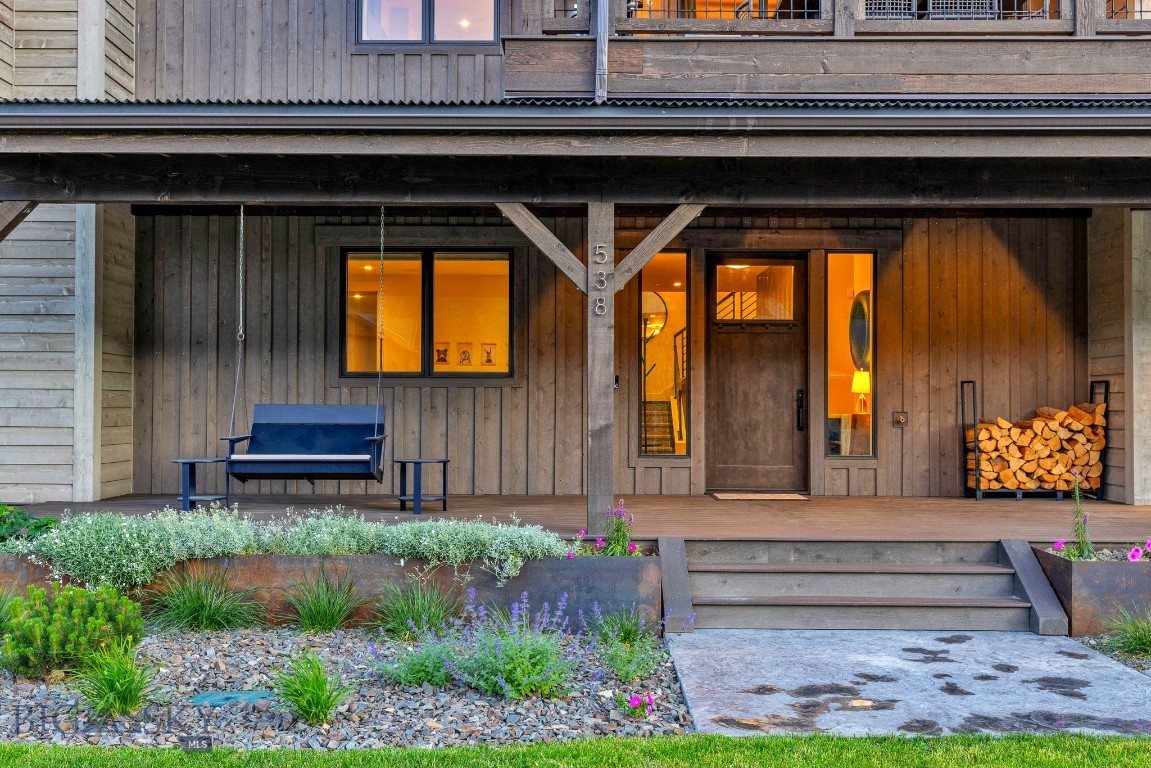 Wood-sided home entrance with a covered porch, blue bench, and stacked firewood.