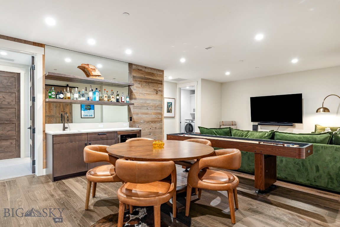 Dining area with a round wooden table beside a built-in bar and green sectional sofa.