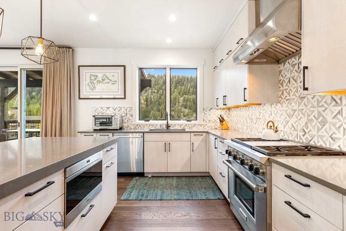 Modern kitchen with white cabinetry, geometric tile backsplash, stainless steel range, and forest views.